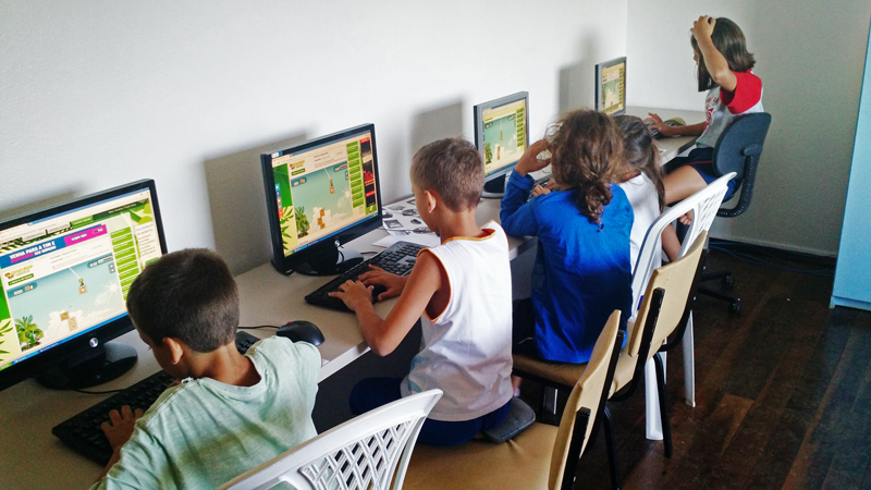 Alunos no laboratório de informática utilizando jogo que aprimora o uso do teclado do computador.